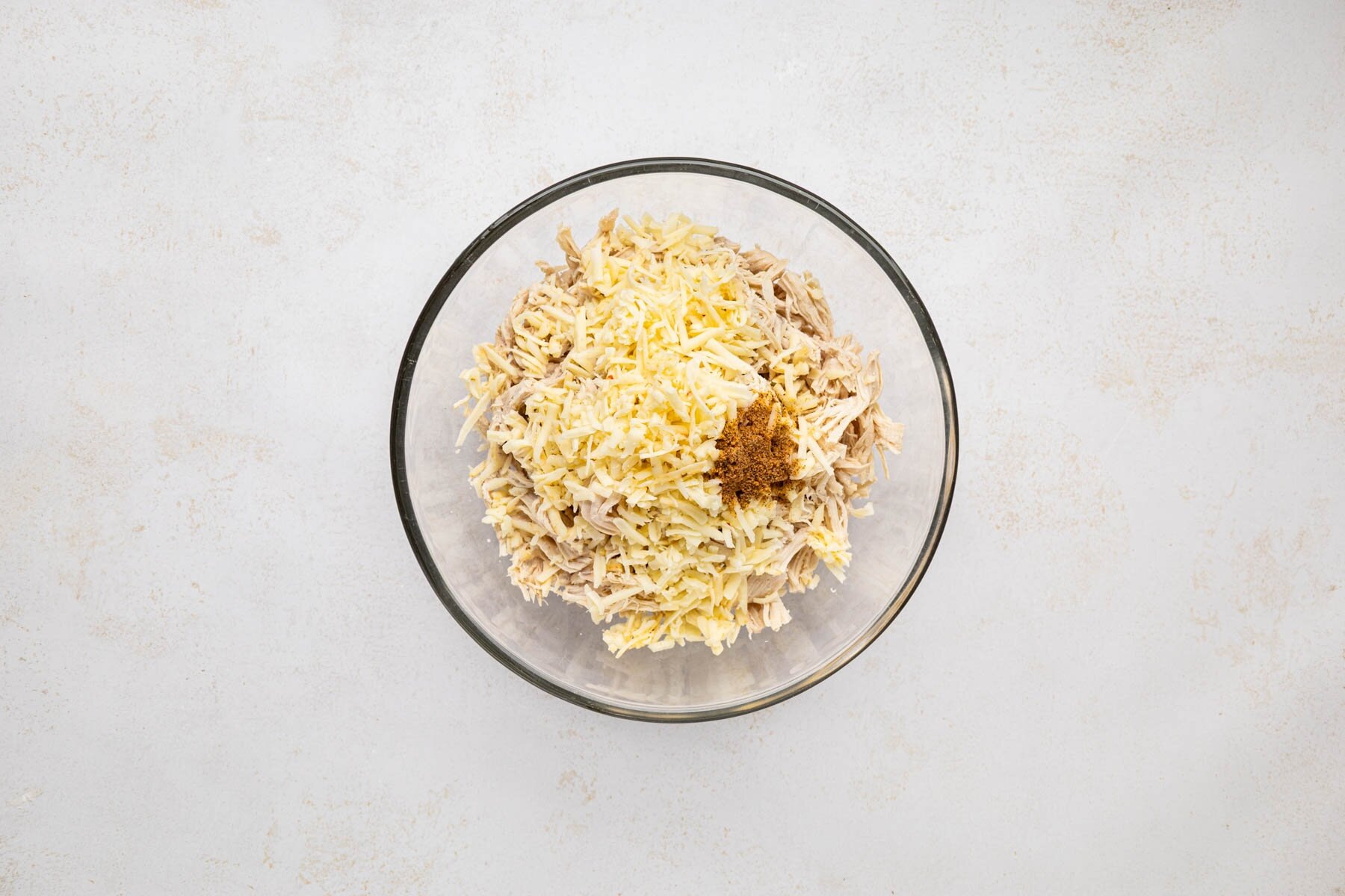 Shredded chicken, cheese, and seasoning added to a bowl.