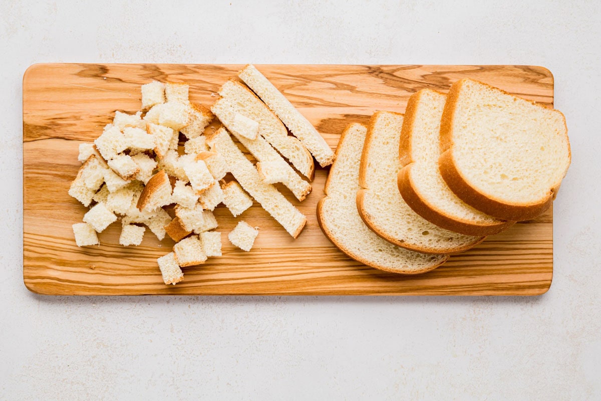 Sliced bread cut into cubes on a wooden cutting board.