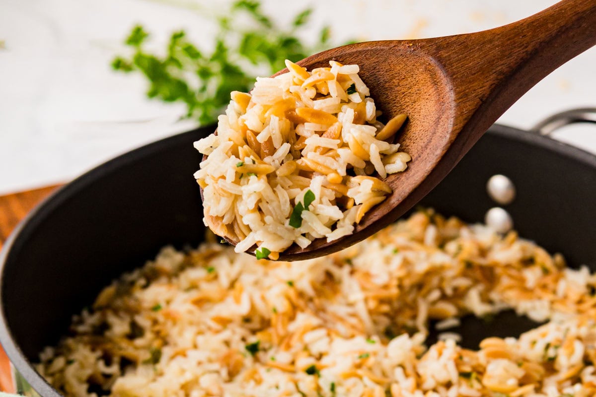 A wooden spoon removing a scoop of rice pilaf from a pan.
