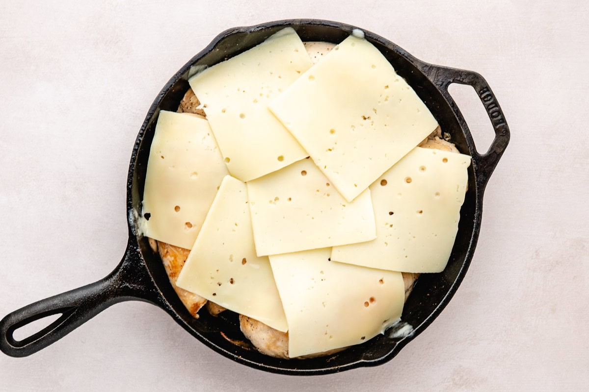 Swiss cheese layered over chicken in a cast-iron skillet.