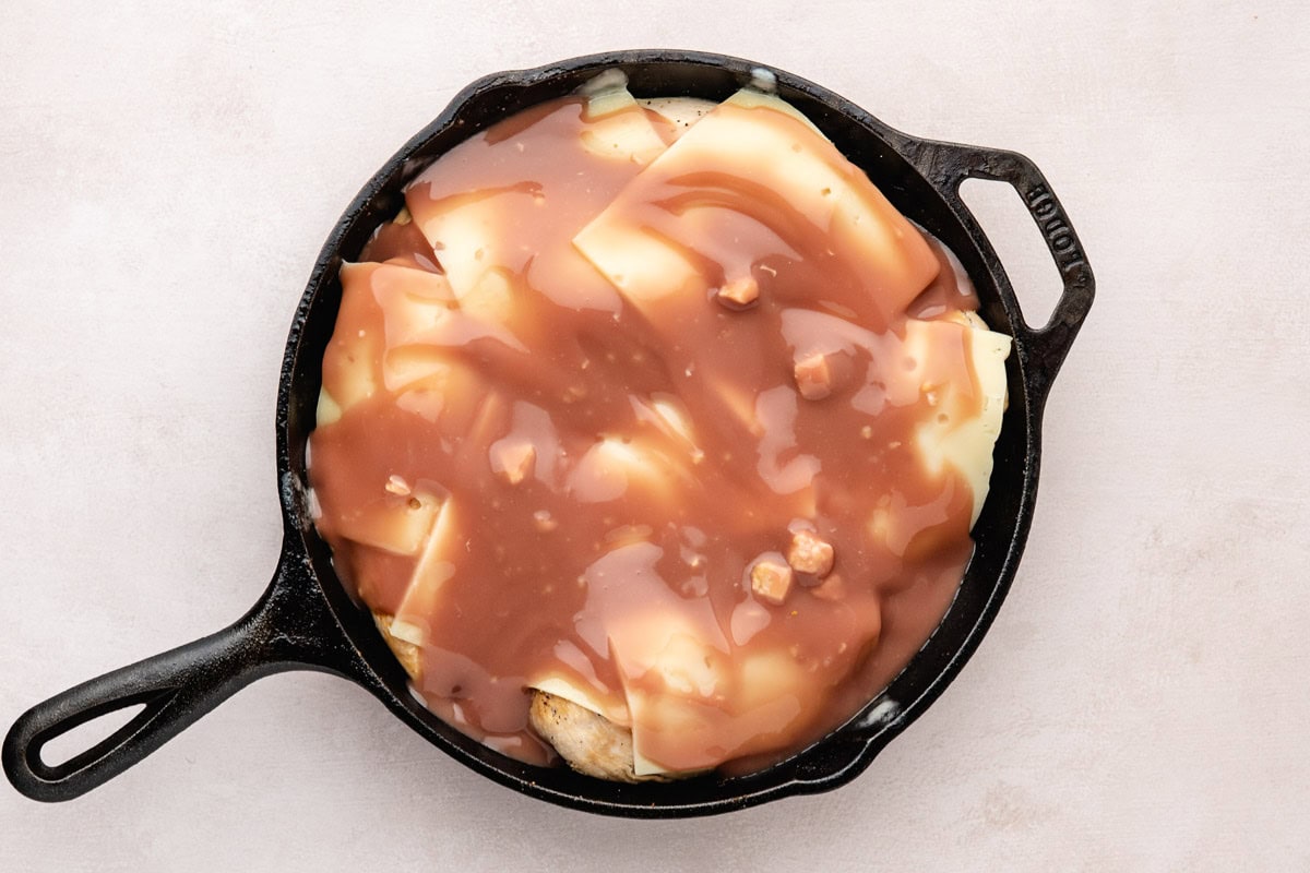 Wine sauce layered over swiss cheese covered chicken in a cast-iron skillet.