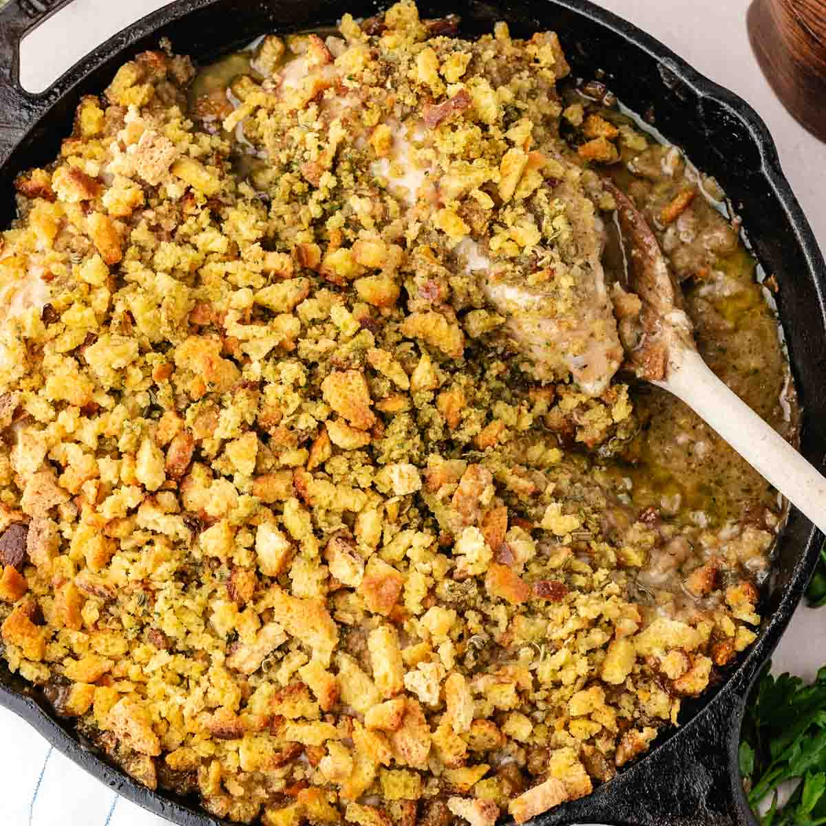 Swiss chicken with wine sauce topped with stuffing in a cast-iron skillet with a spatula removing a serving.