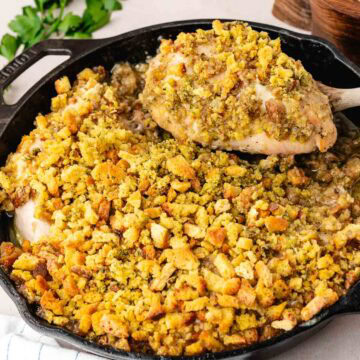 Swiss chicken with wine sauce topped with stuffing in a cast-iron skillet with a spatula removing a serving.