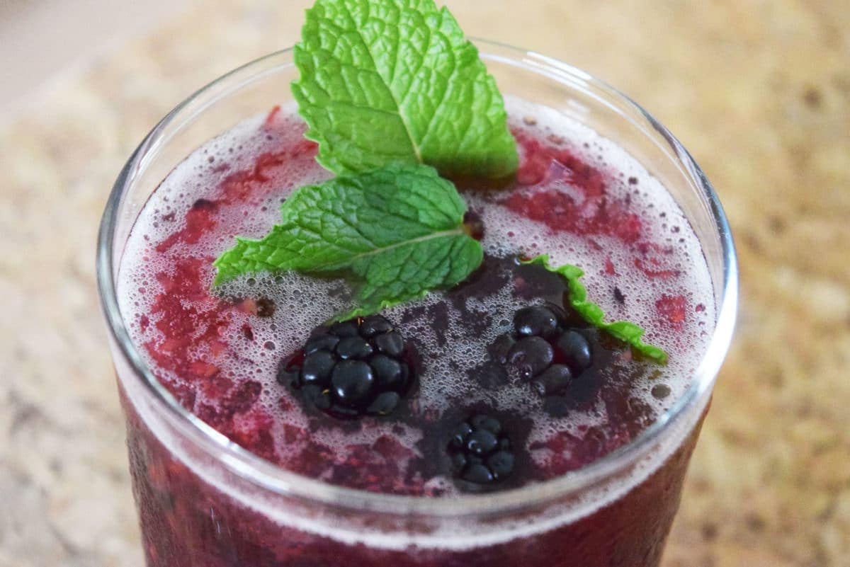 Blackberry bramble cocktail in a glass garnished with fresh blackberries and mint.