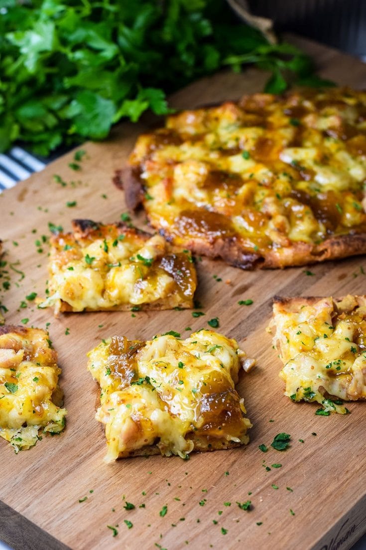 A closeup of a slice of this sausage and fig naan pizza topped with chopped parsley on a wooden cutting board