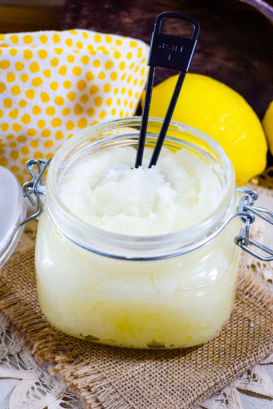 a glass jar of this homemade lemon sugar scrub with a yellow lemon in the background