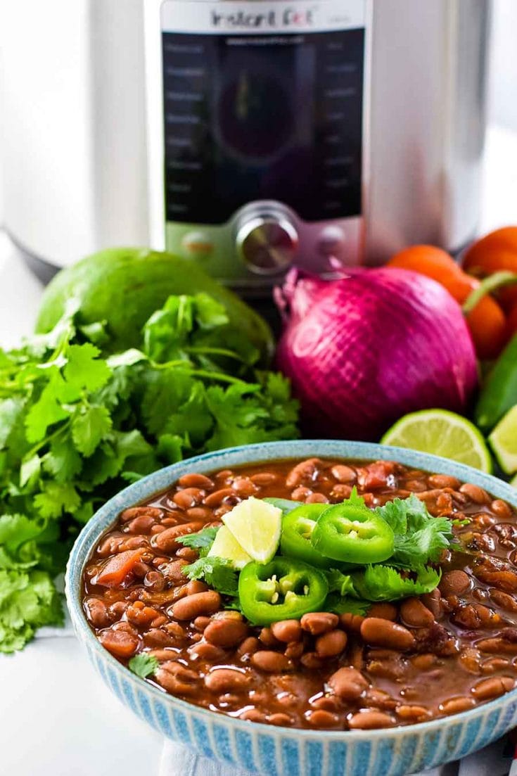 an overhead view of these charro beans made in the instant pot or on the stovetop with the ingredients used to make it in the background