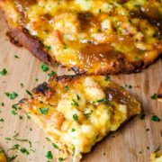 A closeup of a slice of this sausage and fig naan pizza topped with chopped parsley