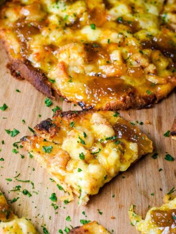 A closeup of a slice of this sausage and fig naan pizza topped with chopped parsley
