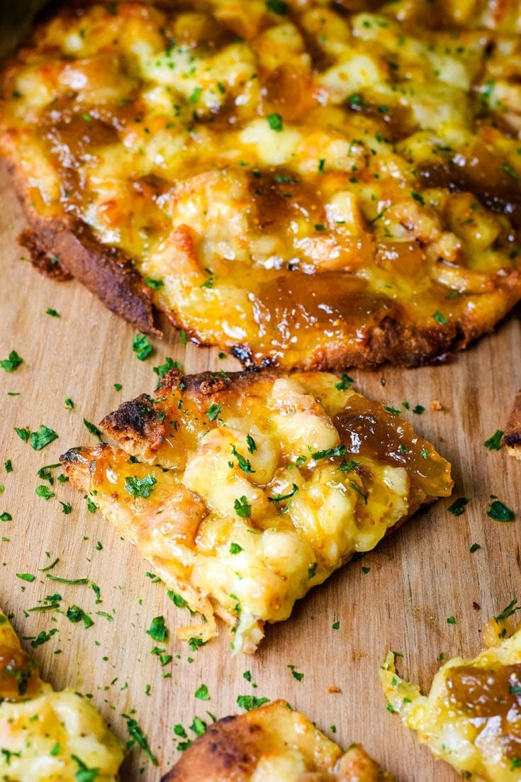 A closeup of a slice of this sausage and fig naan pizza topped with chopped parsley