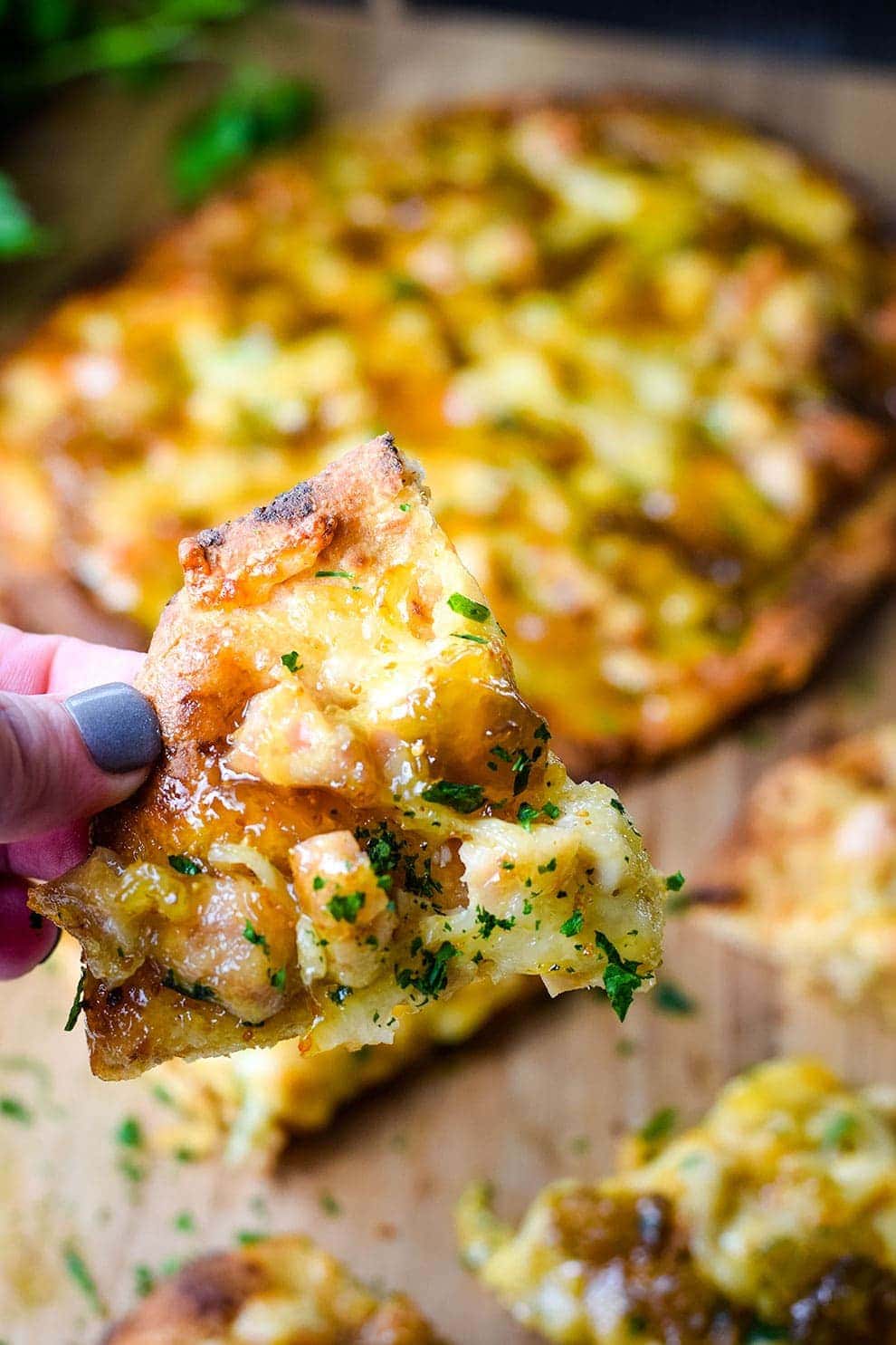 A closeup of a slice of this sausage and fig naan pizza topped with chopped parsley