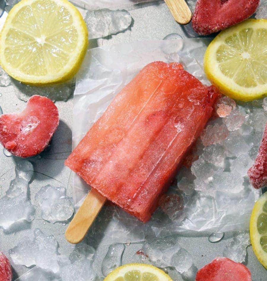 a homemade strawberry lemonade popsicle surrounded by frozen strawberries and lemon slices