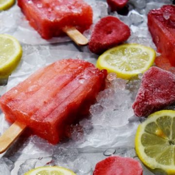 a few homemade strawberry lemonade popsicles on ice cubes with frozen strawberries and lemon slices