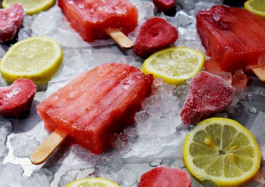 a few homemade strawberry lemonade popsicles on ice cubes with frozen strawberries and lemon slices