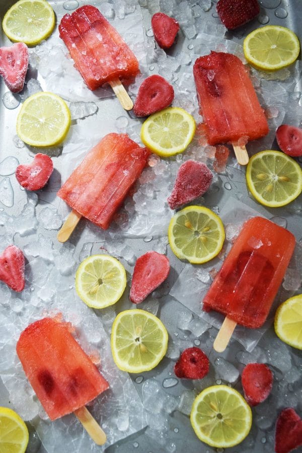 Strawberry Lemonade Popsicles on a tray of ice with lemons and strawberries.