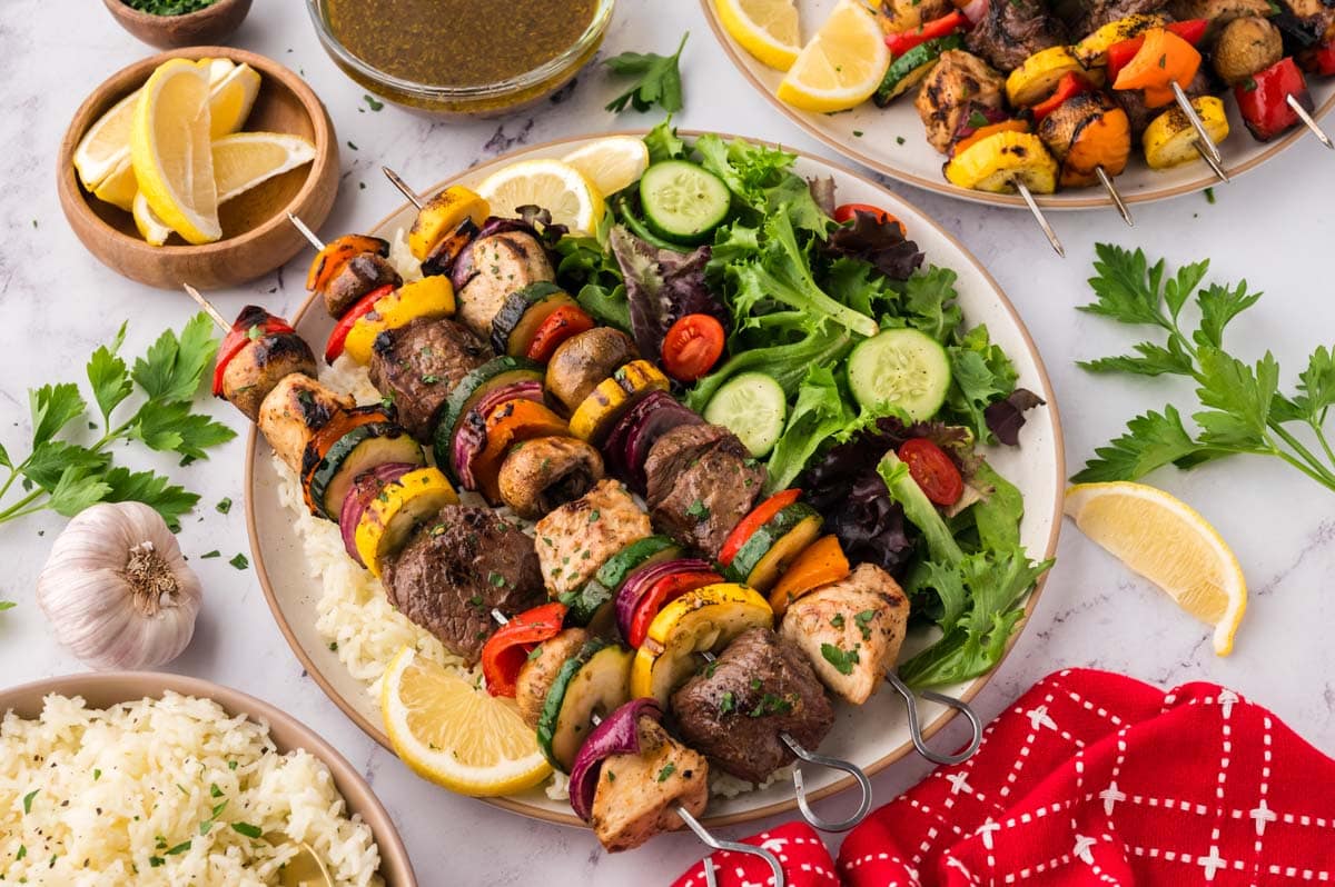 Steak and chicken skewers on a plate with a green salad.