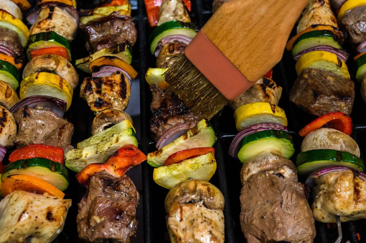 Brushing shish kabob marinade of skewers as they cook on the grill.