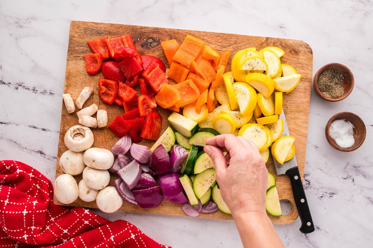 Sprinkling salt and pepper on cut veggies.