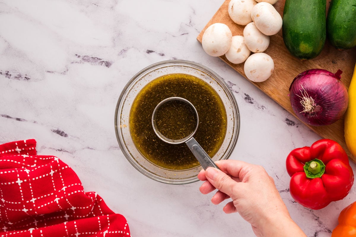 Removing a portion of marinade with a measuring cup.