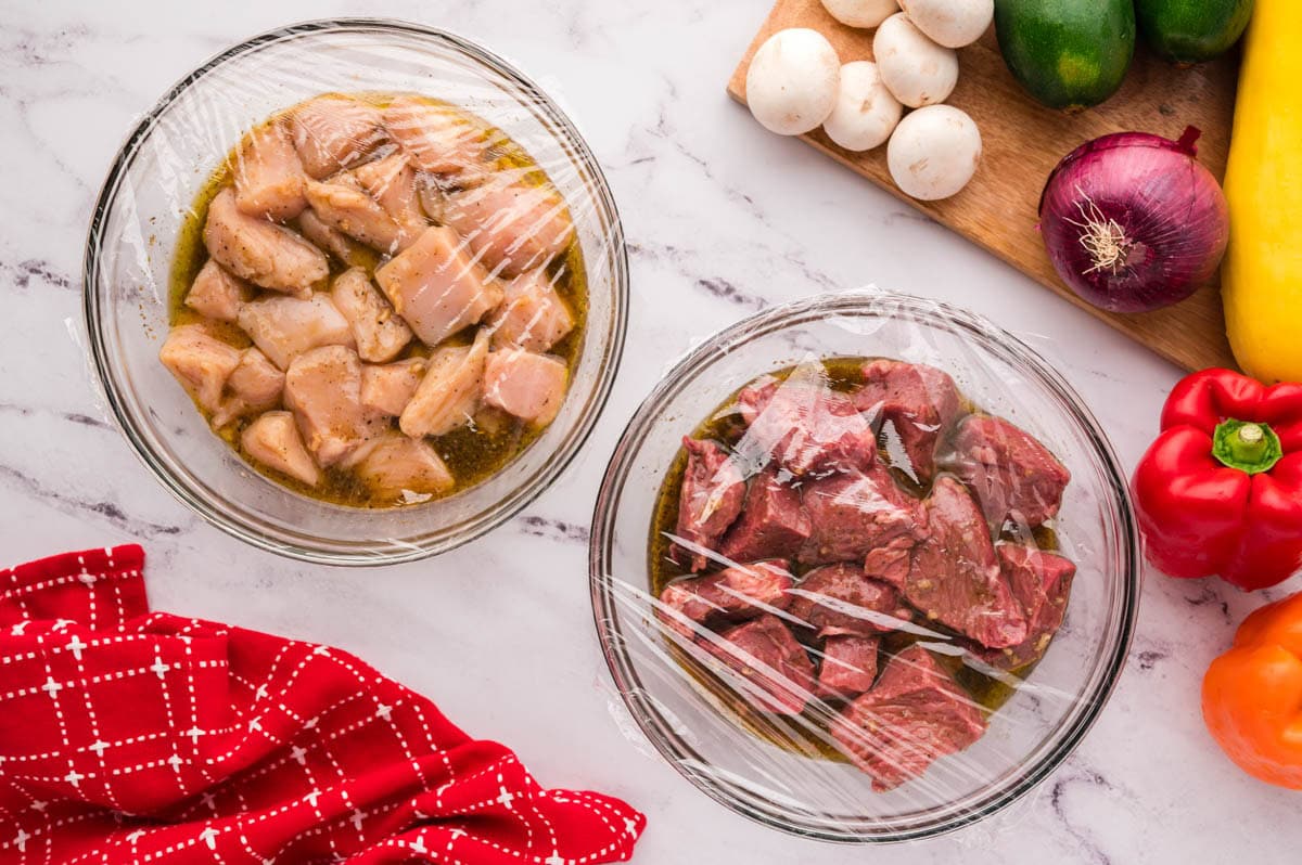 Two separate bowls with chicken and steak marinating in shish kabob marinade.