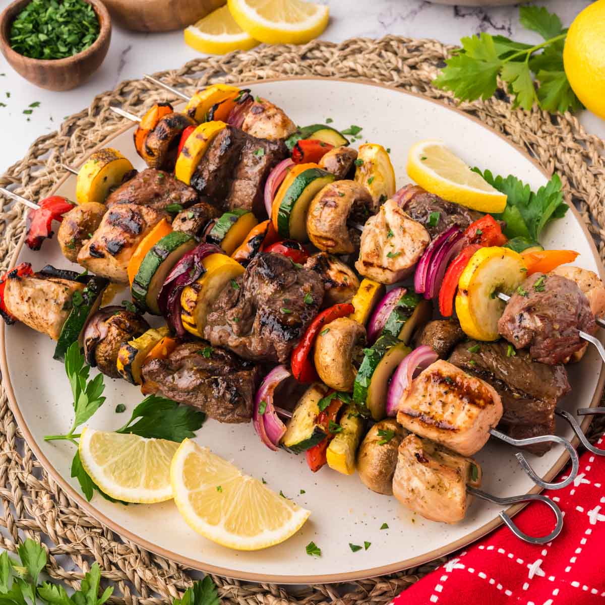 Grilled steak and chicken kabobs with veggies on a plate.