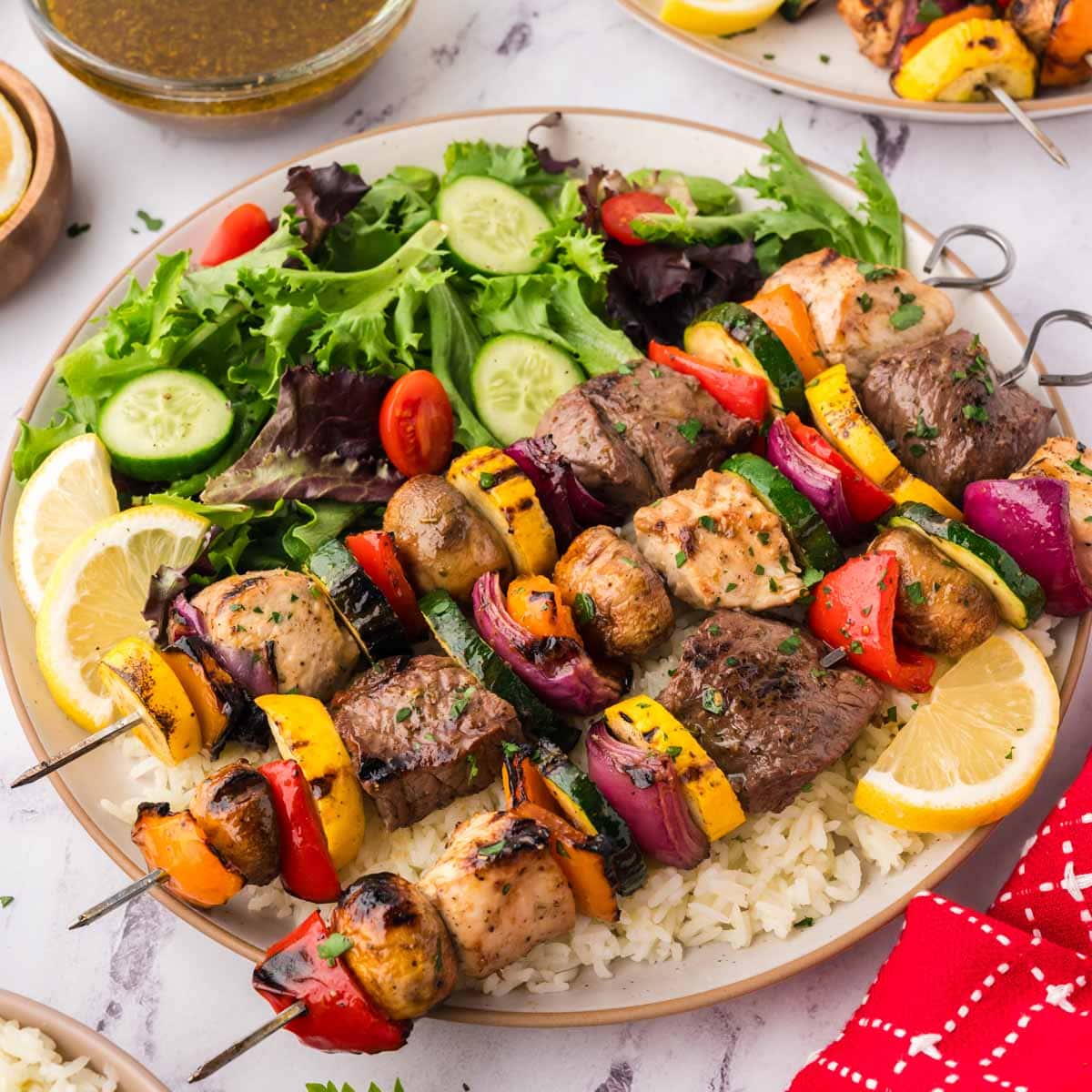 Grilled steak and chicken shish kabobs with veggies on a plate with a green salad.