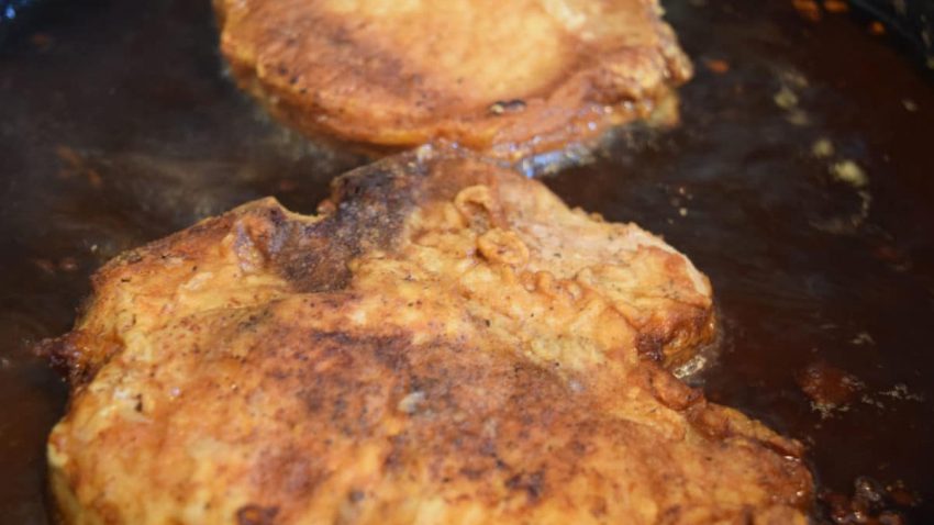 Floured Pork Chop frying in a cast iron skillet