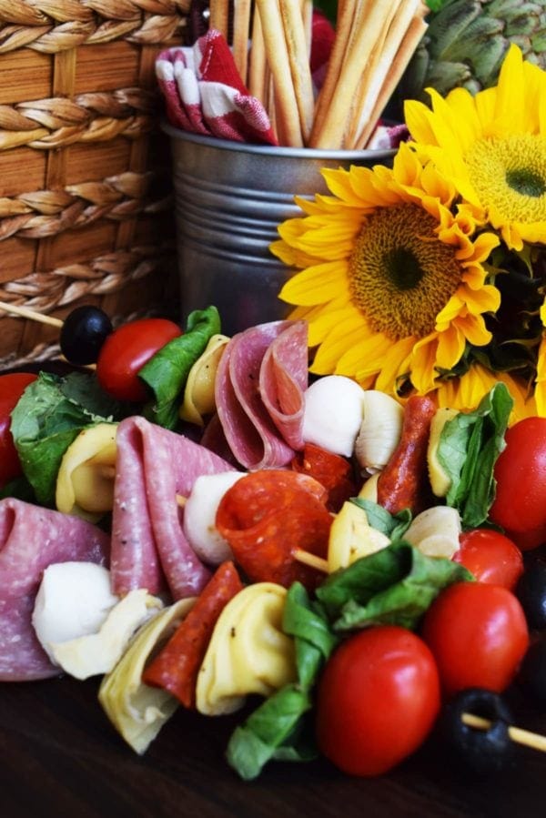 A skewer of tomatoes, cheese, basil, and salami on a tray.