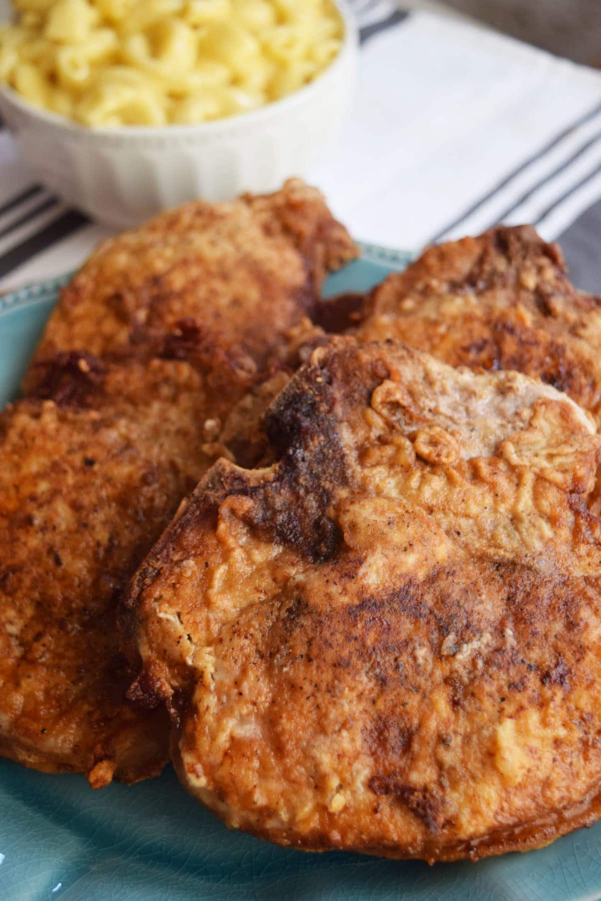 Southern Fried Chops on a turquoise plate set on a table with creamy mac and cheese. 