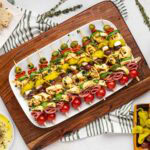 Antipasto skewers on a white serving platter set on a wooden serving board.