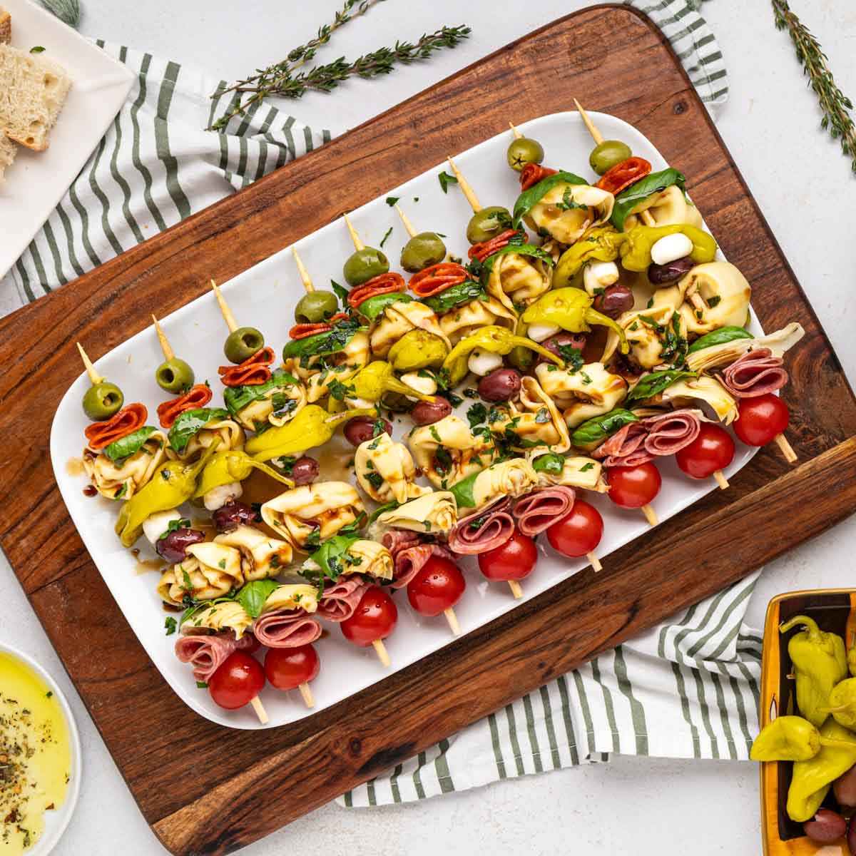 Antipasto skewers on a white serving platter set on a wooden serving board.