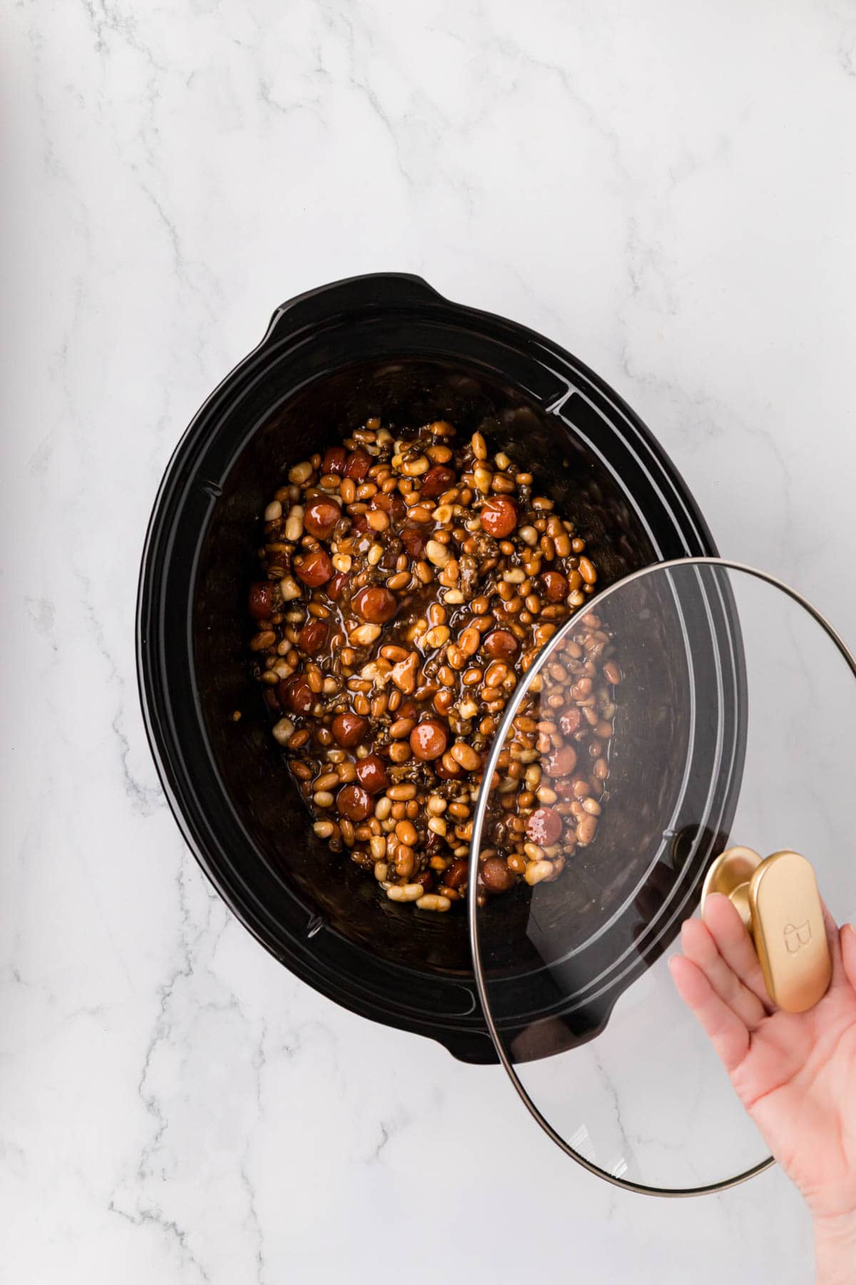 A hand placing a lid on the slow cooker.
