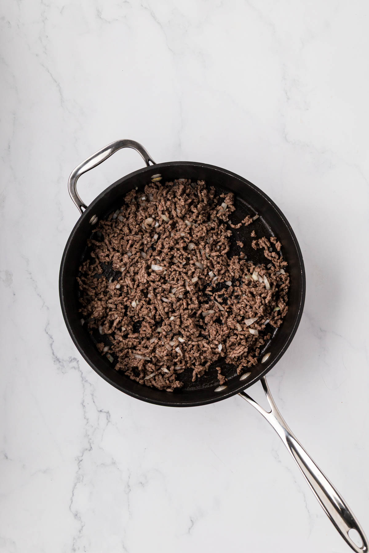 Ground beef cooked in a skillet with onion.