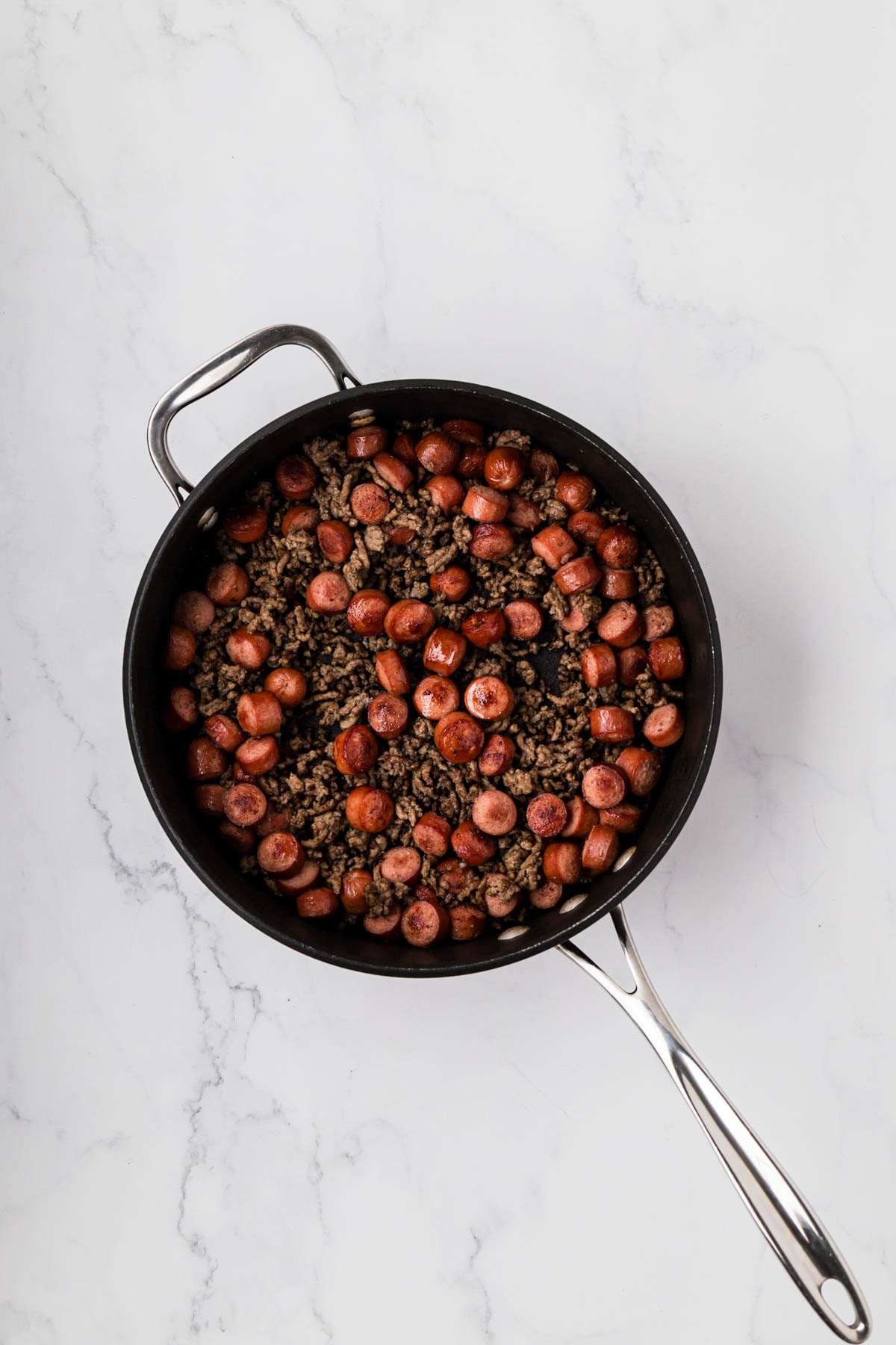 Hot dogs cooked until caramelized in a skillet with ground beef and onions.