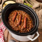 Cowboy Franks and Beans in a slow cooker garnished with full hot dogs on top.