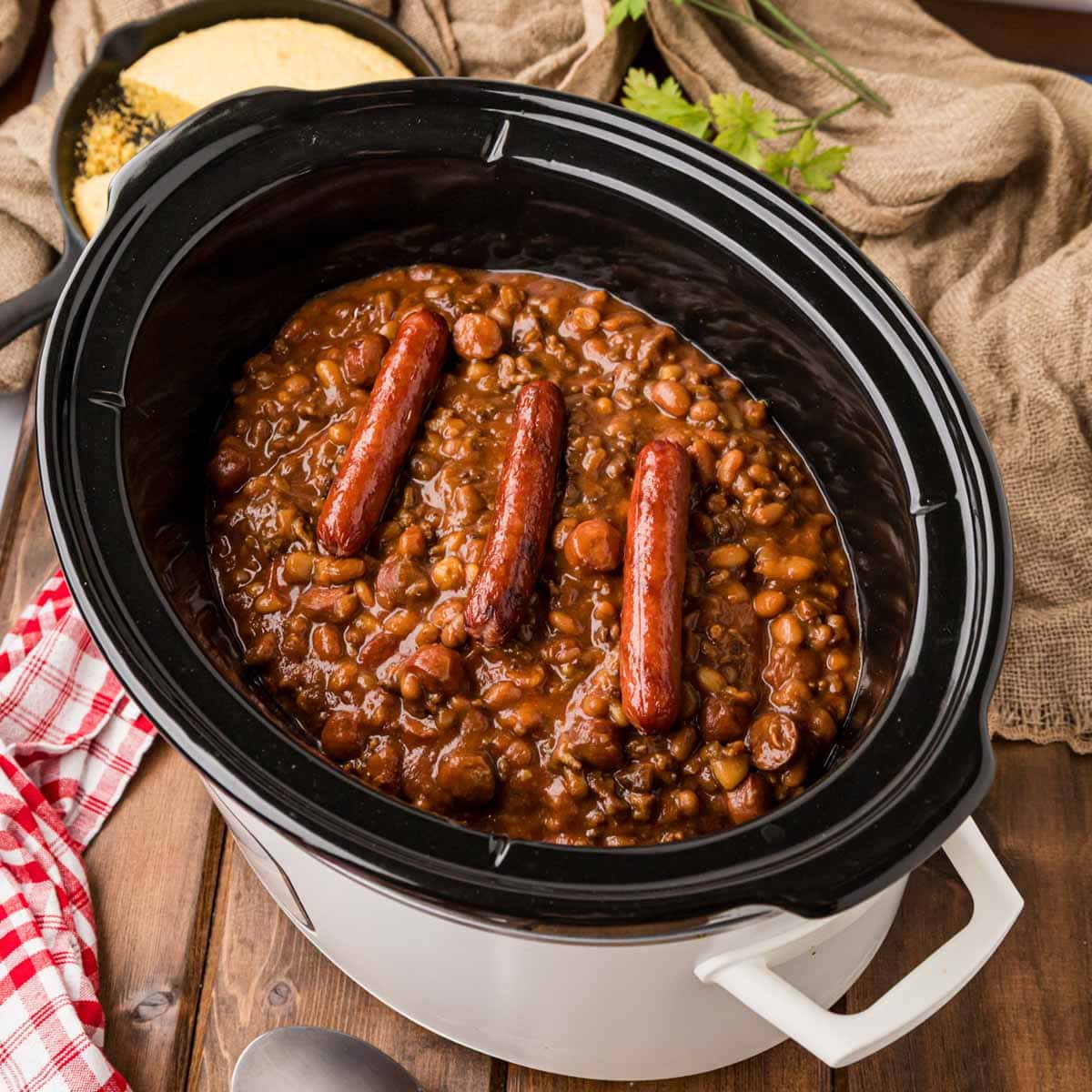 Cowboy Franks and Beans in a slow cooker garnished with full hot dogs on top.