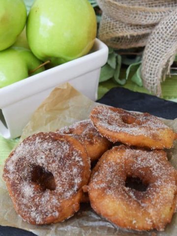some fried green apple rings dusted in cinnamon sugar with a basket of granny smith apples in the background
