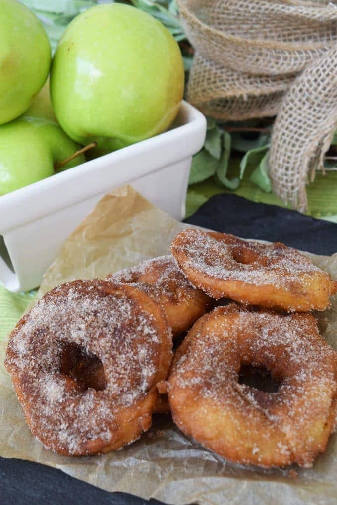 some fried green apple rings dusted in cinnamon sugar with a basket of granny smith apples in the background