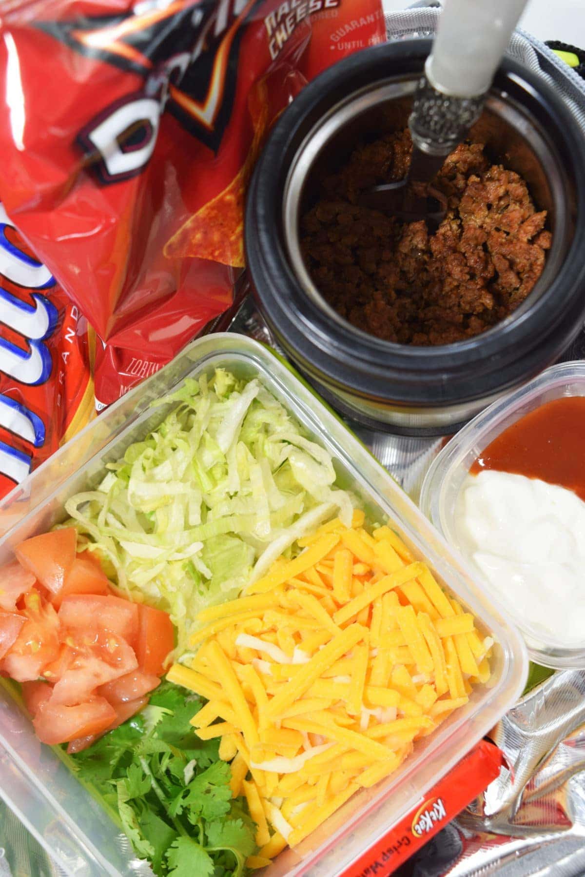 a plastic container filled with the toppings for this walking taco recipe including chopped tomatoes, shredded lettuce, and shredded cheese