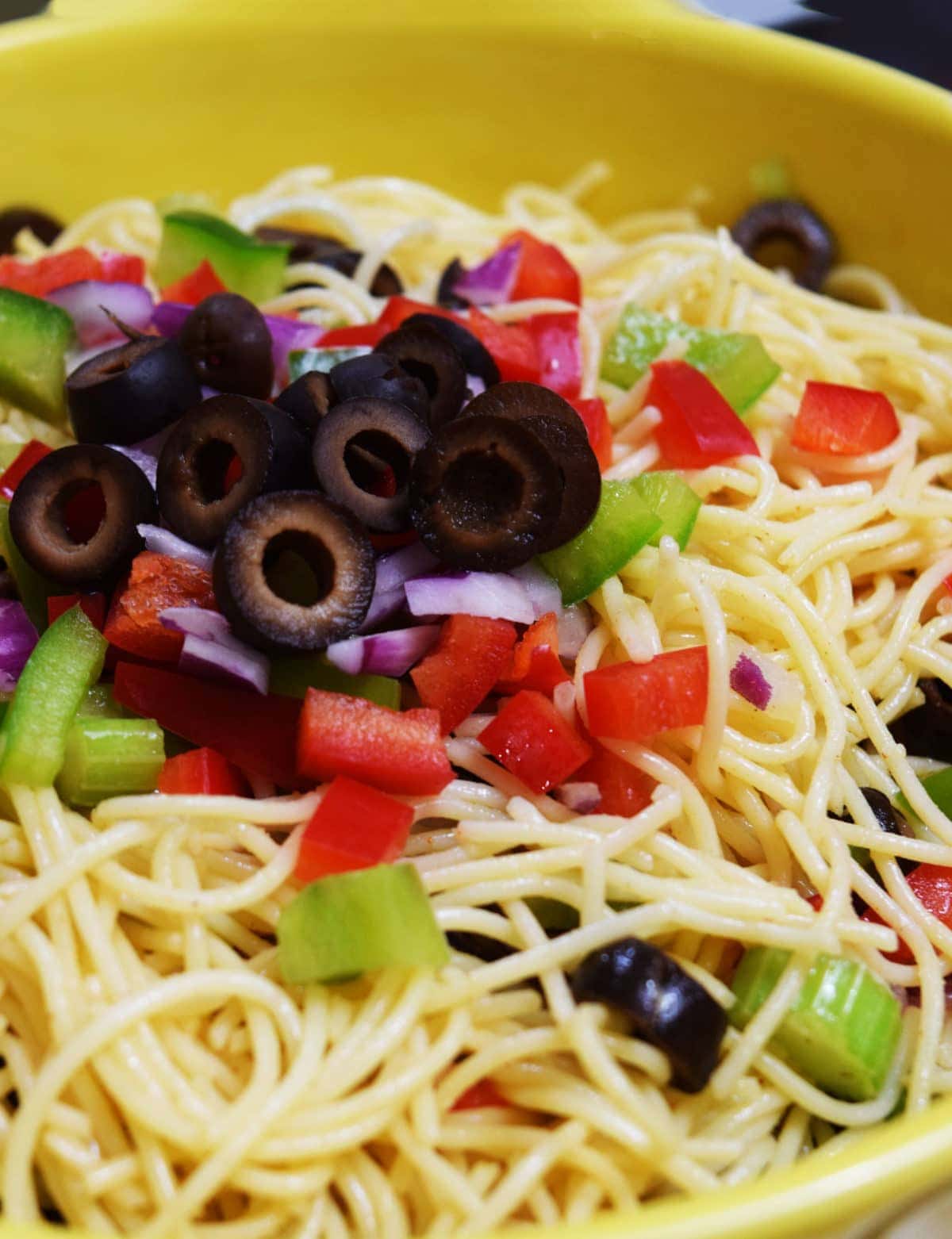 a closeup of a bowl of shelly's pasta salad comprised of spaghetti noodles, black olives, red onion, celery, and red bell pepper