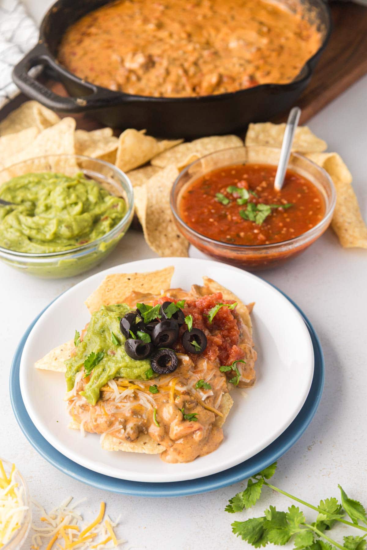 A plate with tortilla chips, topped with queso dip and guacamole, salsa, and black olives.
