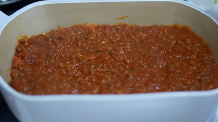 a closeup of the meat and tomato sauce spread on the bottom of a baking dish for this ultimate baked spaghetti recipe