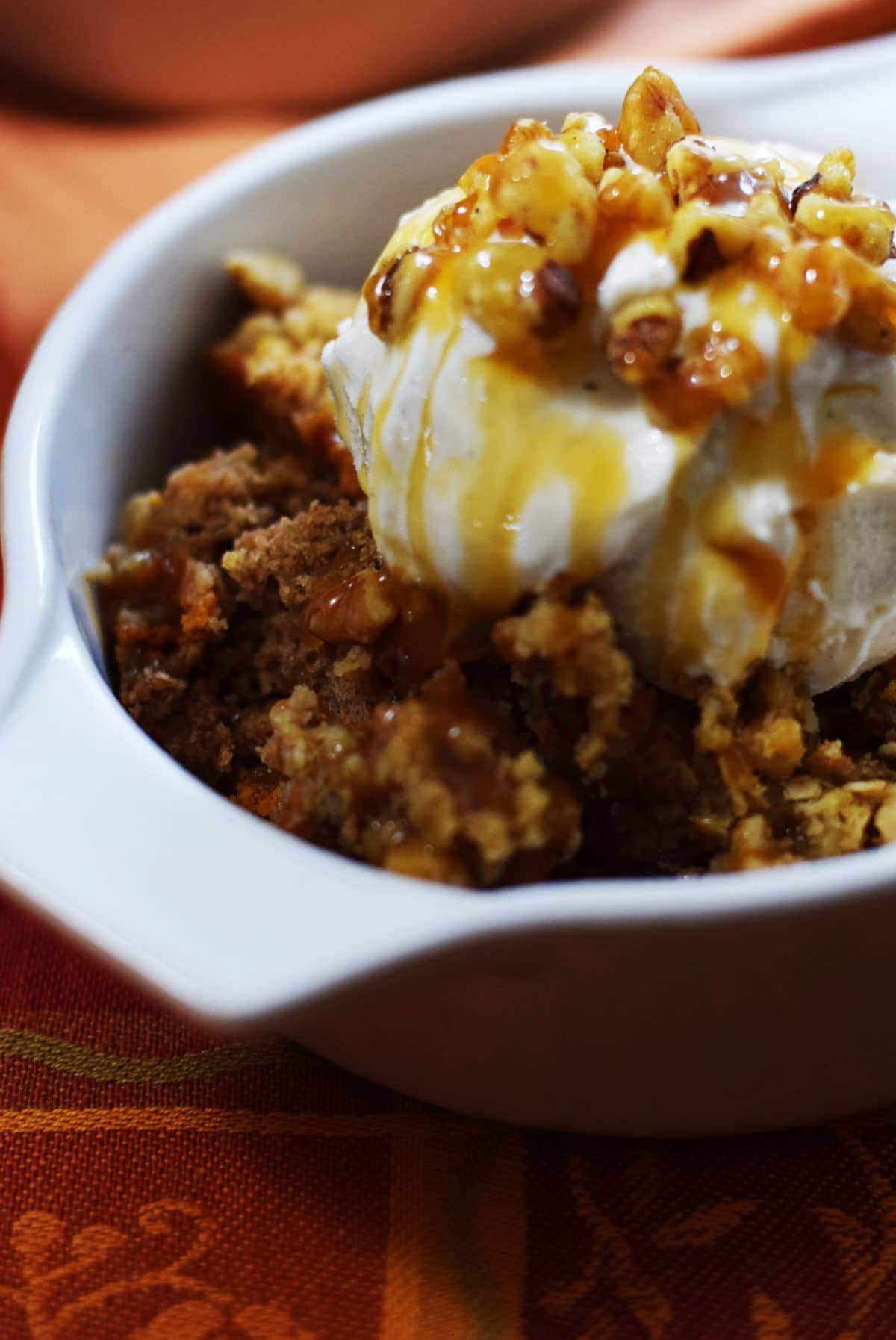 a closeup of a serving of this caramel pumpkin spice crunch cake topped with vanilla ice cream and caramel sauce