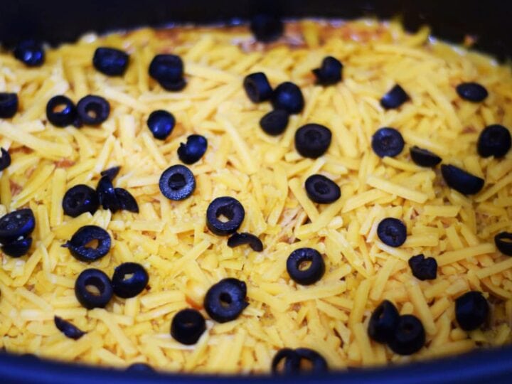 a closeup of shredded cheese and sliced black olives inside of a slow cooker for this crock pot chicken enchilada casserole recipe