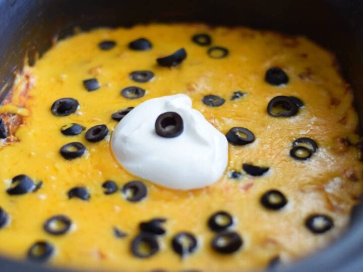 a closeup of shredded cheese and sliced black olives inside of a slow cooker for this crock pot chicken enchilada casserole recipe