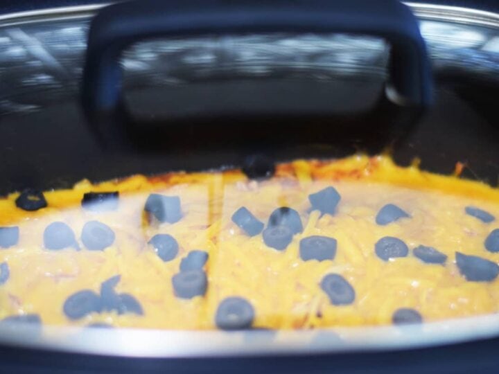 a closeup of shredded cheese and sliced black olives inside of a slow cooker for this crock pot chicken enchilada casserole recipe