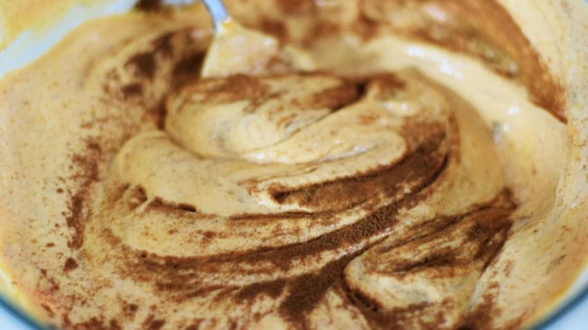 the raw batter of this caramel pumpkin spice crunch cake being swirled with ground cinnamon
