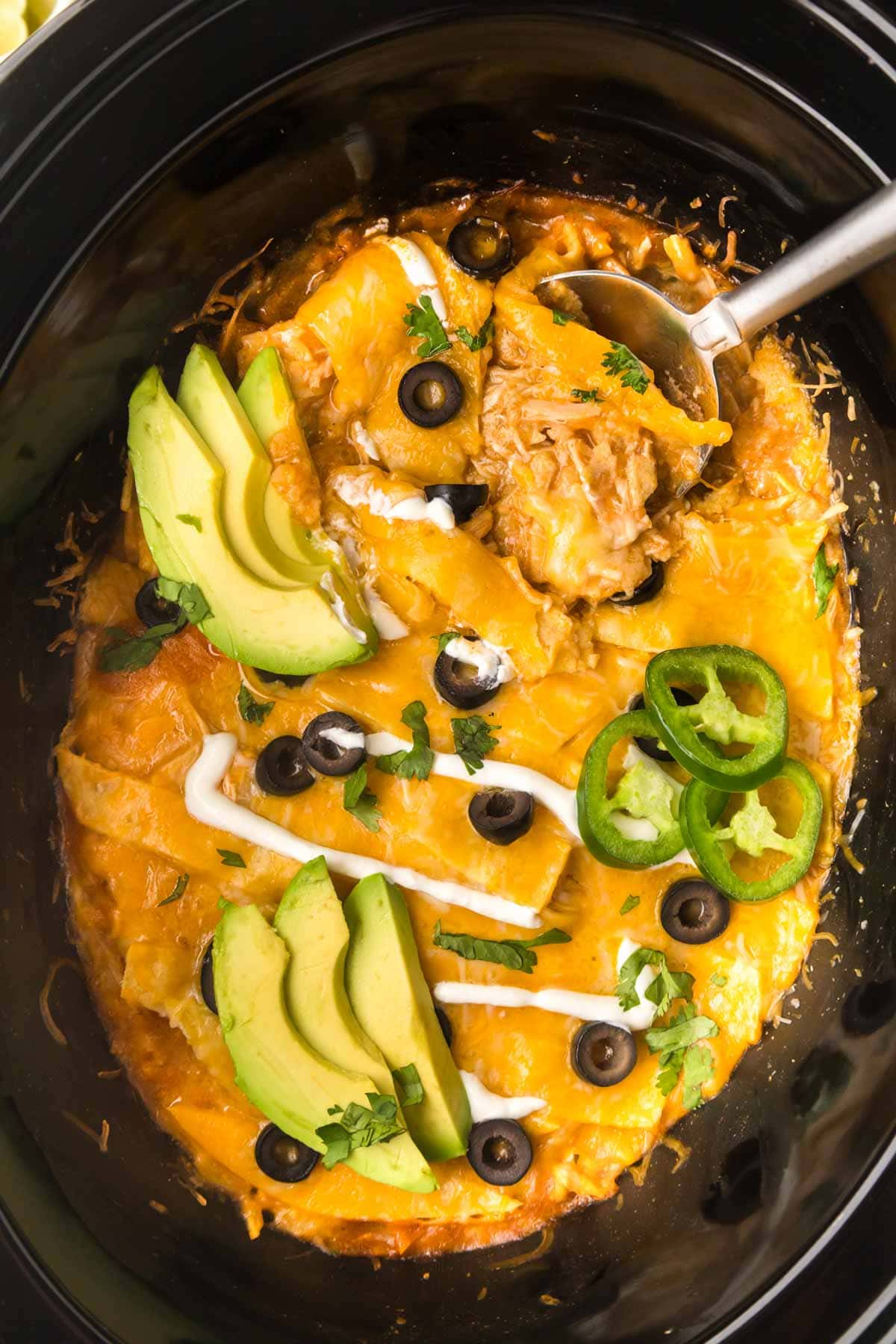 A spoon scooping out a serving of slow cooker enchilada casserole.