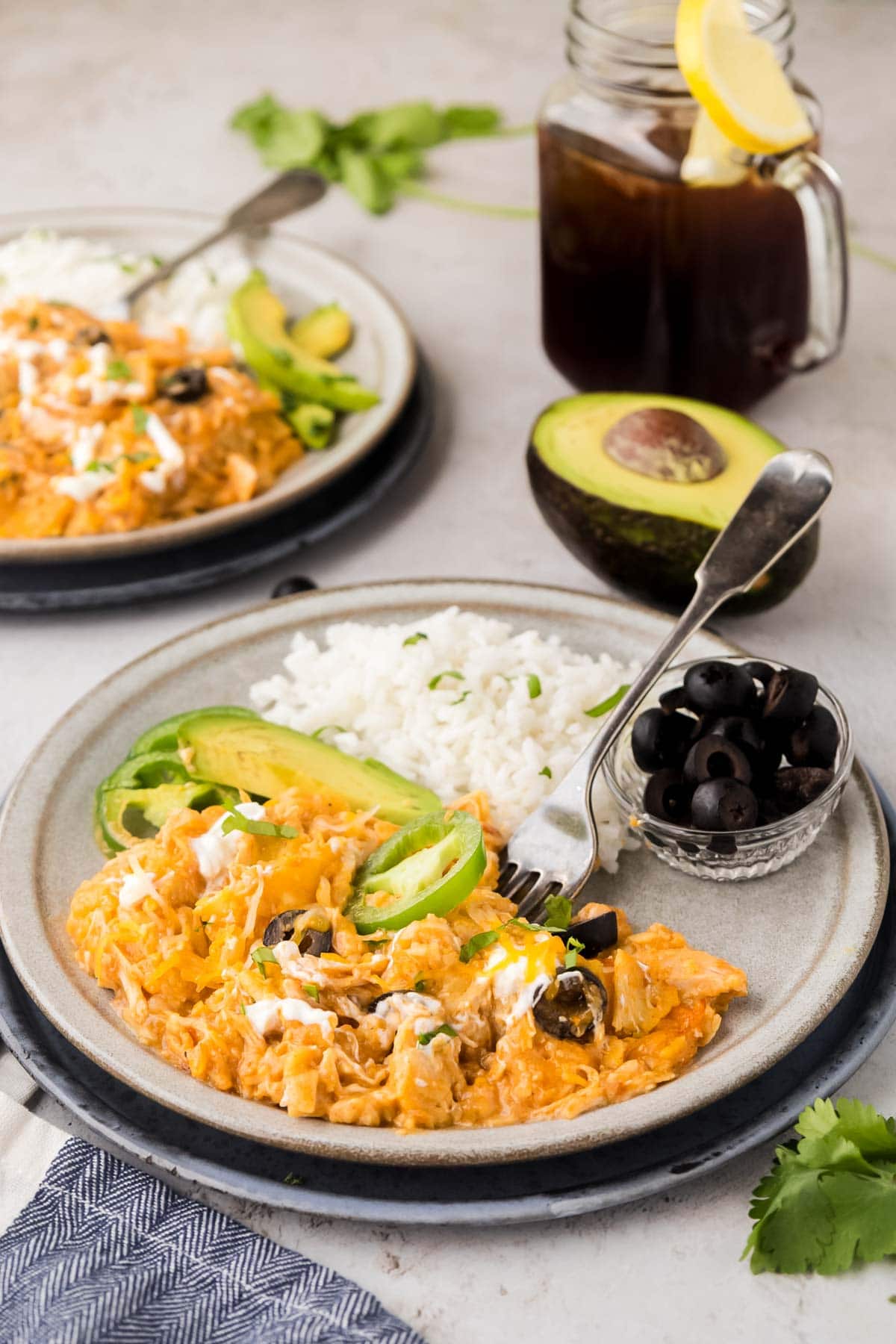 A plate with enchilada casserole, rice with black olives and avocado and jalapeno slices.