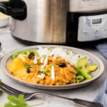 A plate with enchilada casserole made in the slow cooker, rice with black olives and avocado and jalapeño slices.